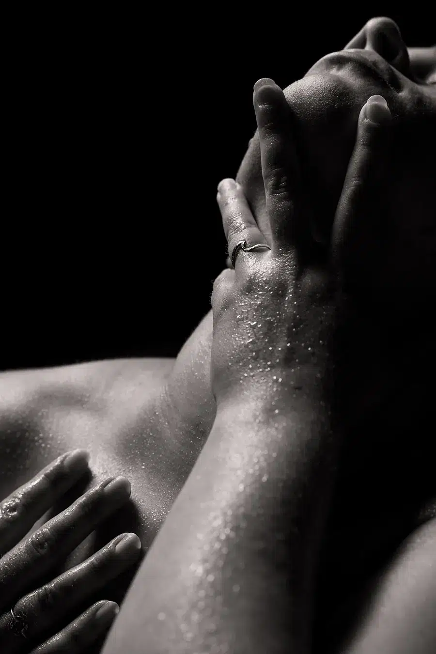 A close-up black and white photo of a person with wet skin, one hand covering their mouth and chin, and another hand resting on their shoulder.